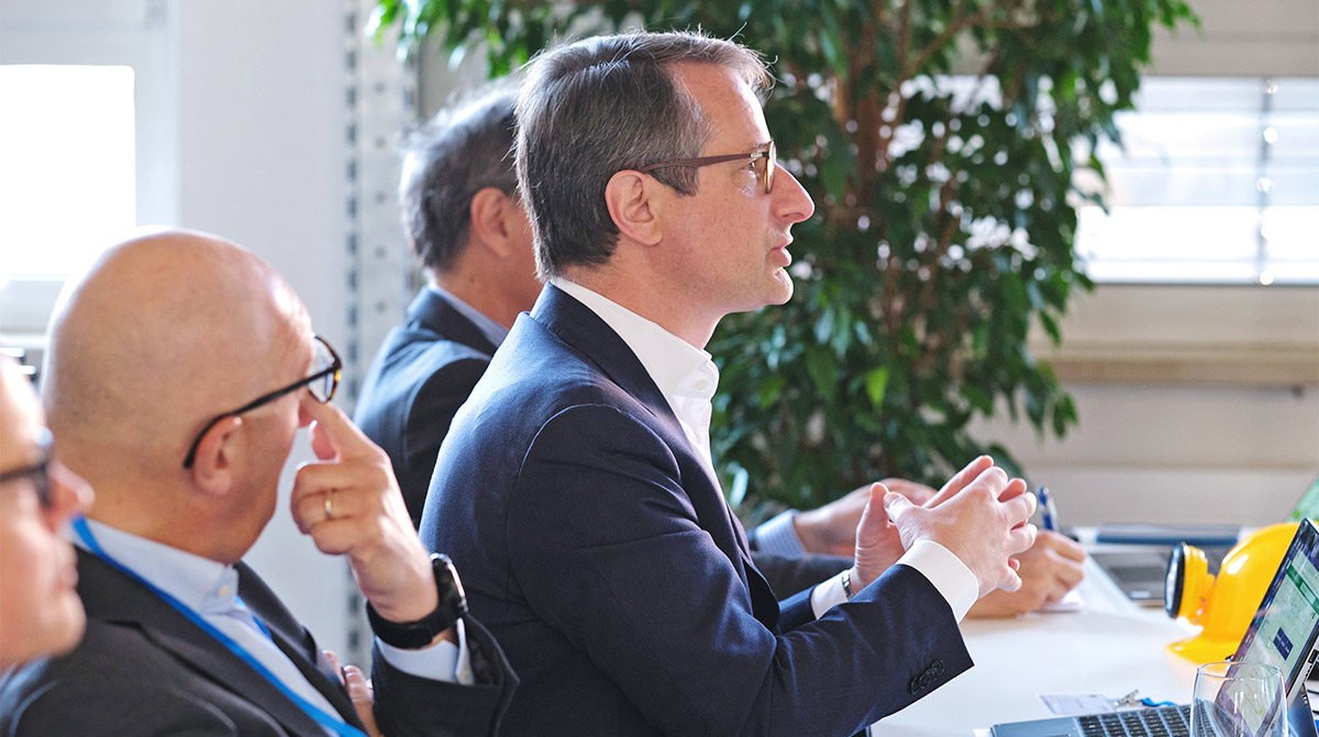 A man speaks while sitting at the table and other people are around him.