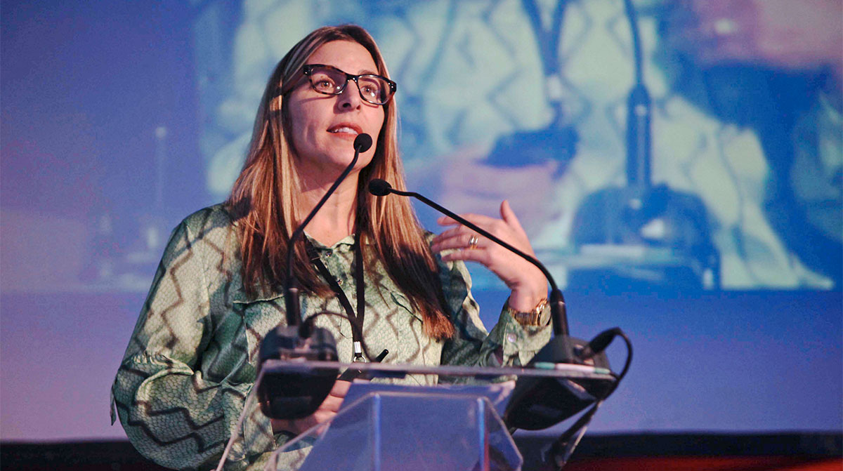 A woman stands at the lectern and gestures with her hands.