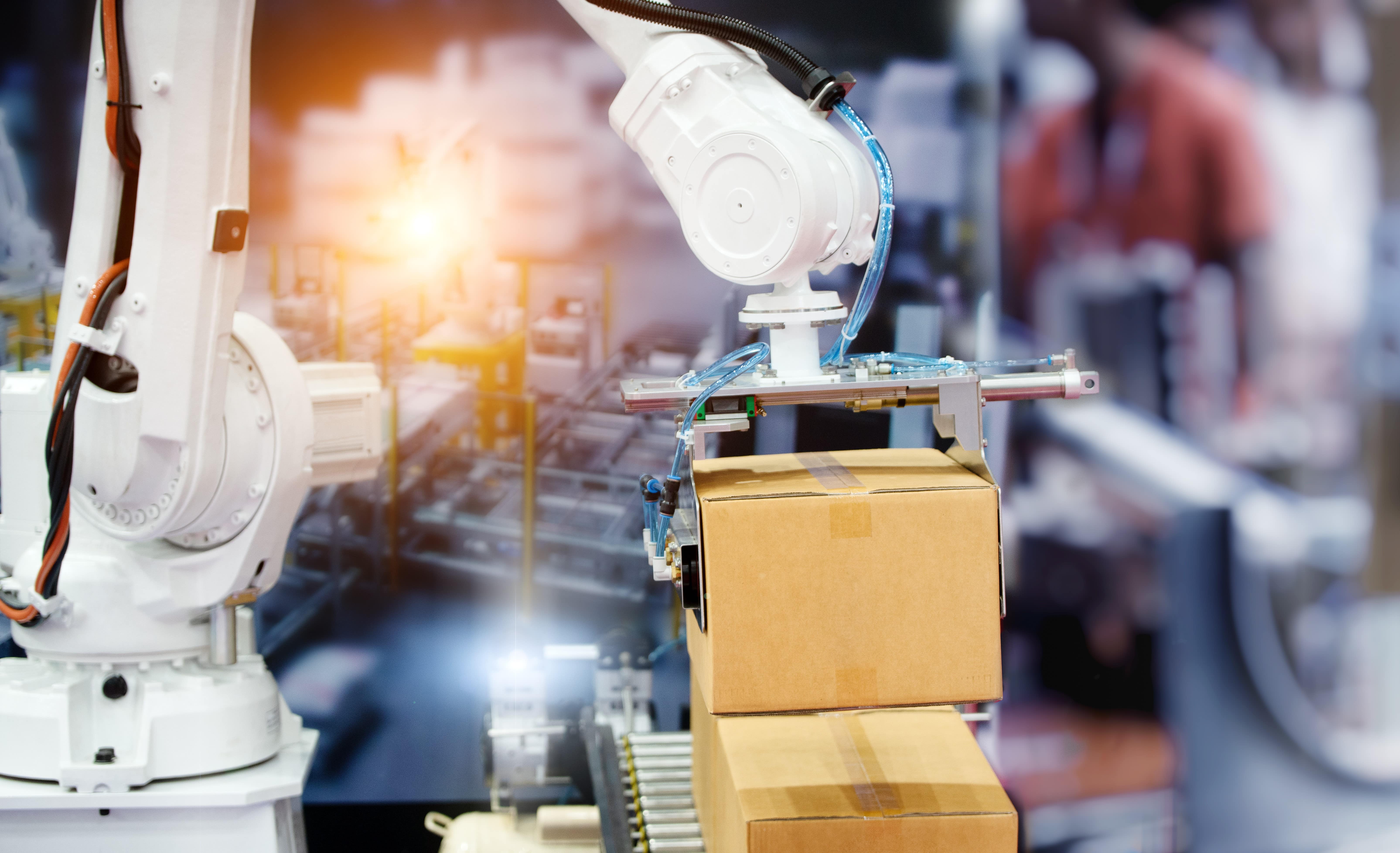 Ein Robotorarm hält eine Verpackungsbox, vor dem Hintergrund einer Fabrikhalle