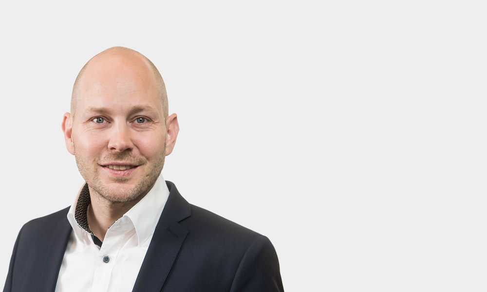 Christopher Eckert, Senior Consultant Portraetfoto von Christopher Eckert vor grauem Hintergrund